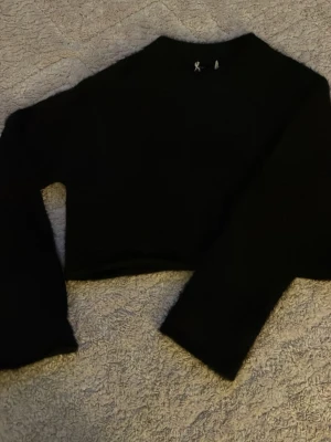 Svart croppad fluffig tröja - Säljer en svart croppad tröja med lång ärm och fluffig, pälsliknande yta. Tröjan har en enkel rund halsringning och är perfekt för dig som gillar en mjuk och cozy vibe. Passformen är loose och materialet känns riktigt gosigt mot huden.