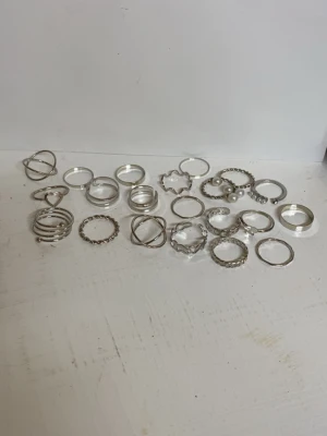 Snygga silvriga ringar i olika former - Säljer ett set med flera silvriga ringar i olika coola designer, bland annat vågig ring, hjärtan och en med fjäril. Ringarna är tunna och trendiga, perfekta att mixa och matcha. Materialet är metall med silvrig finish och vissa har pärldetaljer. Inte äkta silver!