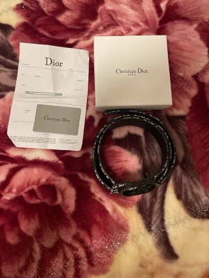 Svart och vit rutig Dior väst - Säljer en snygg väst från Christian Dior med svart och vit rutig design och breda axelpartier. Västen har ett klassiskt Dior-mönster och är tillverkad i en mix av skinn och textil. Perfekt för dig som vill sticka ut med en exklusiv look.