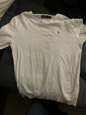 Vit tröja från Polo Ralph Lauren - Vit långärmad tröja från Polo Ralph Lauren med klassisk rund hals och diskret logobroderi på bröstet. Tröjan är tillverkad i mjuk bomull och har ribbade muddar vid hals och nederkant. Perfekt för en clean och stilren look.