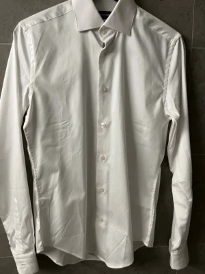 Dressman skjorta  - Tjena! Säljer denna stilrena vita skjortan från Dressmann i mycket bra skick. Passar perfekt till både vardag och fest. Storlek: XS (35/36). Vid frågor är det bara att kontakta mig 🤩
