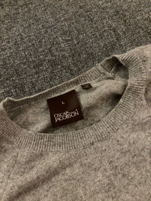 Grå tröja Oscar Jacobson - Säljer en stilren grå rundhalsad tröja från Oscar Jacobson, modell Gustaf Roundneck. Perfekt för dig som gillar klassisk och enkel desig