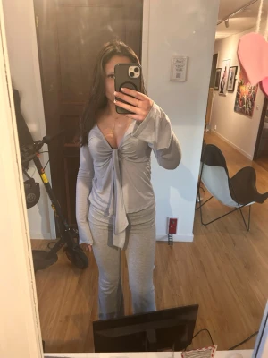 Ljusgrå långärmad omlottopp med knyt - Säljer en ljusgrå långärmad topp med omlottkänsla och knyt framtill. Toppen har djup v-ringning och vida ärmar, vilket ger en chill och trendig vibe. Perfekt att styla med jeans eller mjukisbyxor.