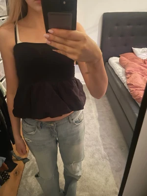 Svart volang topp  - Säljer en svart linnetopp med smala justerbara axelband och volang nedtill. Toppen är croppad och har en luftig passform. Passar också jätte bra som balongkjol. 💕