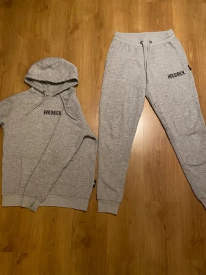 Grå mjukisbyxor från Hoodrich - Säljer ett par grå mjukisbyxor från Hoodrich med svart logotyp på vänster lår. Byxorna har snörning i midjan och ribbade muddar vid bensluten. Materialet är mjukt och bekvämt, perfekt för chill eller träning. Klassisk loose passform och stilren design.