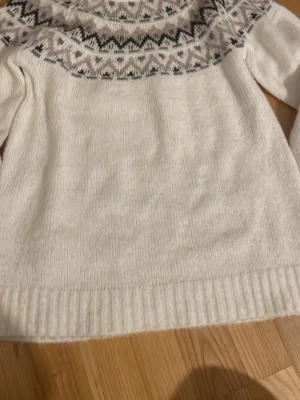 Vit stickad tröja  - Mysig vit stickad tröja från 157 med rund hals och ett snyggt mönster i grått och beige över bröstet och axlarna. Perfekt för kalla dagar och har ribbade muddar vid ärmslut och nederkant. Passar dig som gillar klassisk vinterstil. Knappt använd då den är förstor 