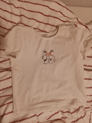 Vit t-shirt med körsbär från Lindex - Vit t-shirt från Lindex med ett sött körsbärstryck och en liten rosett broderad framtill. 🍒✨️Rund hals och korta ärmar, tillverkad i mjuk bomull. Perfekt för dig som gillar enkla men gulliga detaljer på dina kläder. 20 kr+ frakt( eller 2 t-shirts för 30 kr)❤️💰