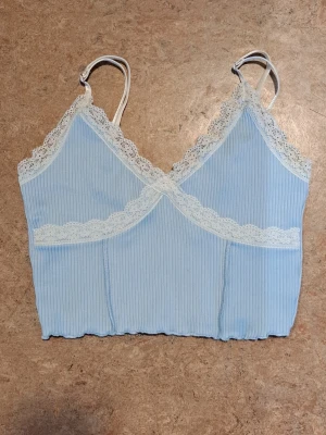 Ljusblå ribbad linnetopp från H&M - Supersöt ljusblå linnetopp från H&M Divided i storlek S. Toppen har justerbara axelband och är dekorerad med vit spets.