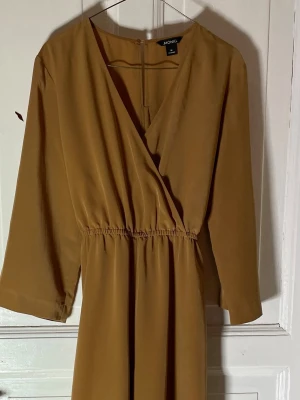 Beige byxdress från Monki med omlott - Säljer en beige byxdress från Monki i storlek M. Modellen har omlottdesign med v-ringning, resår i midjan och ett matchande bälte. Materialet är mjukt och har ett snyggt fall. Ärmarna är trekvarts och benen är raka och vida. Perfekt för dig som gillar stilrena plagg. Mått: byst: 45 cm midja: 37 cm längd: 133 ben innermått: 66 cm ärm innermått: 34 cm djur finns i hemmet. 