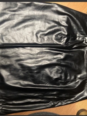 Svarta skinnkjol från Gina Tricot - Snygga svarta skinn kjol från Gina Tricot med raka ben och diskreta fickor både fram och bak. kjolen har en glansig finish och dragkedja i sidan.