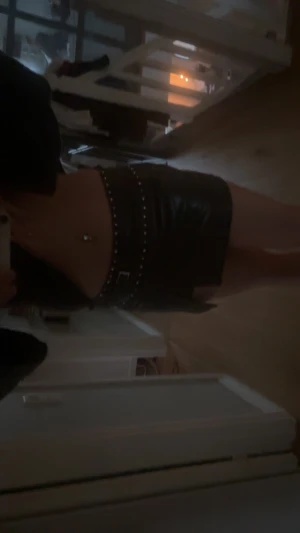 Svart kort kjol i skinn med nitar - Säljer en svart kort kjol i skinnimitation med coola silverfärgade nitar längs midjan och ett bälte med spänne. Kjolen har en liten slits framtill och sitter tight i midjan. Det finns även inbyggda shorts i kjolen som inte syns! Helt ny, säljer då jag köpte dubbelt