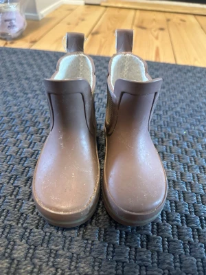 Bruna/ beiga  gummistövlar st 20 - Säljer ett par bruna gummistövlar  med rund tå och platt sula. Skorna har dragflik baktill och elastiska paneler på sidorna för enkel påtagning. Insidan är fodrad med ljus textil. Perfekt för regniga dagar och höstväder.