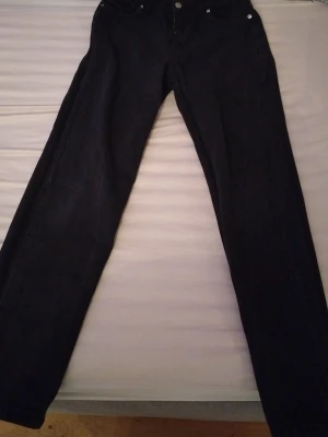 Svarta loose fit jeans från RYVLS - Svarta jeans från RYVLS i loose fit-modell, tillverkade i 100% bomull. Klassisk femficksdesign med silverfärgade knappar och urban stil. Passar dig som gillar avslappnad look och vill ha bekväma jeans med lite extra utrymme.