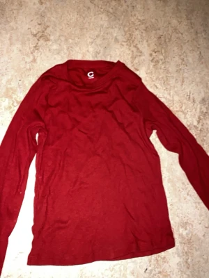Röd långärmad topp från C - En enkel och stilren röd långärmad topp från C i storlek 158/164. Toppen har rund halsringning och är gjord i ett mjukt och stretchigt material som känns skönt mot huden. Perfekt att matcha med jeans eller kjol för en clean look.
