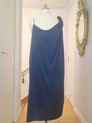 Mörkblå asymmetrisk klänning från ACNE - Säljer en marinblå långklänning med oneshoulder-design och tunna axelband. Klänningen har en avslappnad passform och ett brett, draperat axelband som ger en cool och modern look. Perfekt för dig som gillar stilrena och unika plagg.