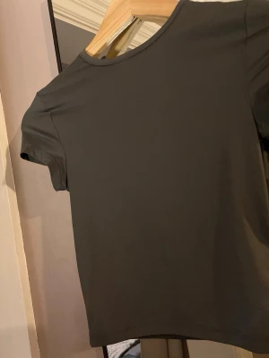 Mörkgrå croppad t-shirt - En stilren mörkgrå croppad t-shirt med rund hals och korta ärmar. Perfekt till gymmet. T-shirten har en tight passform och är tillverkad i ett mjukt material som känns skönt mot huden.