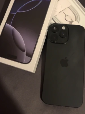 Svart iPhone 16 Pro max box - Säljer en svart iPhone 16 Pro med stilren matt finish och kantig design. Telefonen har tre stora kameralinser på baksidan och levereras i originalkartong med laddkabel och simverktyg. Perfekt för dig som vill ha senaste modellen från Apple.