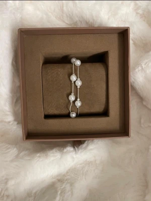 Silverarmband med vita pärlor - Snyggt armband i silverfärgad metall med dubbla tunna kedjor och vita pärlor. Armbandet har en stilren och elegant design som passar till både vardag och fest! Obs: boxen på bilden följer inte med! 