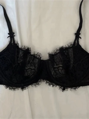 Svart spets-bh med rosetter - Snygg svart spets bh från VICTORIA SECRET. Aldrig använd men har klippt av lappen. Den är i storlek 70b. Säljer den då jag beställde fel storlek. Bh:n har tunna axelband med rosetter och fina spetsdetaljer längs kanterna. Ställ gärna frågor och kika gärna på de andra sakerna jag säljer💗💕obs lånad bild, men kan skicka egna💕