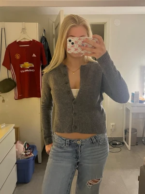 Grå kofta från Zara - Mysig grå kofta från Zara med rund halsringning och knäppning framtill. Koftan är ribbstickad vid ärmslut och nederkant och har en klassisk, rak passform. Perfekt att slänga över en topp eller t-shirt.