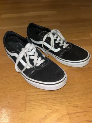 Svarta Vans Old Skool sneakers - Klassiska Vans Old Skool sneakers i svart med vit sula och vit sidostrip. Skorna har snörning och är tillverkade i mocka och canvas. Perfekta för en avslappnad och cool stil. Bra skick. 