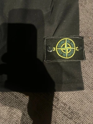 Svart T-shirt  - En snygg svart T-shirt med ett svart gult  märke på sida 