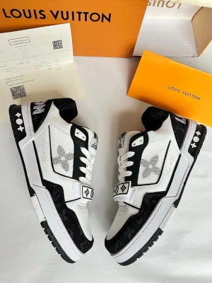 Louis Vuitton svartvita sneakers - Snygga svartvita Louis Vuitton sneakers med klassiska monogramdetaljer och kontrasterande paneler. Skorna har snörning, rund tå och platt sula. Tillverkade i en mix av skinn och syntetmaterial med tydliga LV-loggor på sidan och tungan.