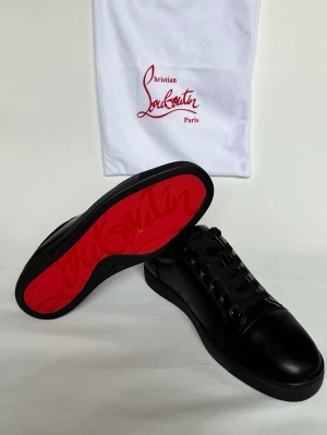 Svarta sneakers från Christian Louboutin - Stilrena svarta sneakers från Christian Louboutin i skinn med klassisk röd sula och snörning. Diskret design med rund tå och svarta detaljer, perfekt för dig som gillar exklusiva och tidlösa sneakers.