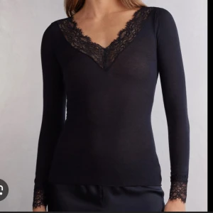 Intimissimi topp - Säljer en svart långärmad topp med v-ringning och fina spetsdetaljer vid halsringningen och ärmsluten. Toppen har en slim passform och är perfekt för dig som gillar en elegant och stilren look. Från Intimissimi. Prövad. Inte använd. Inga lappar kvar
