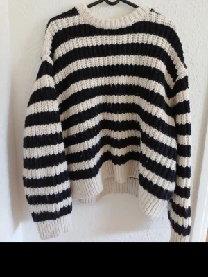 Randig stickad tröja i svart och vitt - Säljer en chunky stickad tröja med breda svarta och vita ränder. Tröjan har rund hals, långa ärmar och ribbstickade muddar. Materialet ät mjukt och mysigt.