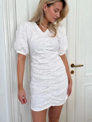 Vit studentklänning  - Superfin vit kort klänning med puffärmar och v-ringning. Klänningen har en strukturerad, rynkad design och markerad midja som ger en snygg siluett. Perfekt för student!🌼 Aldrig använd, nypris 1000kr men slutsåld.