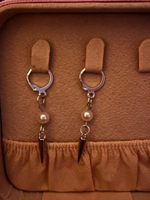 Silvriga örhängen med pärla och spike - Säljer ett par coola örhängen i silverfärgad metall med hängande vita pärlor och spetsiga spikes. Örhängena har en modern design med runda hoops och detaljer som ger en edgy vibe. Perfekta för dig som gillar att sticka ut med dina accessoarer.