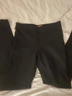 Svarta kostymbyxor från Lindex - Snygga svarta kostymbyxor från Lindex Premium Punto. Byxorna har en klassisk rak/bootcut passform med pressveck framtill och medel hög midja. Matrialet är mjukt och stretchigt. 