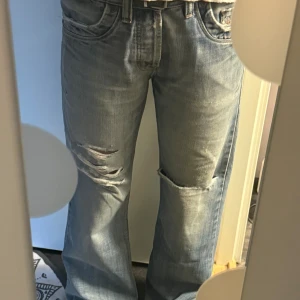 Ljusblå slitna jeans från Diesel - Artikelnummer EGB200001. Storlek 30, L32.  Ljusblå jeans från Diesel med slitningar och hål på benen för en rå look. Klassisk femficksmodell med bruna detaljer på bakfickorna och bootcut-snitt. Tvättas i 30°. Diesel jeans 93243 ca 25594. 06627-6112. cif a2 a62226170. mod cardel L32.
