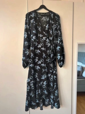 Pernilla Wahlgren - Svart omlottklänning från Pernilla Wahlgren med blått och vitt blommönster. Klänningen har långa ärmar med lätt puff och knyt i midjan. Perfekt för dig som gillar en feminin och bekväm stil. Sparsamt använd💕