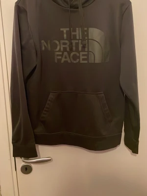 Svart hoodie från The North Face - Säljer en svart hoodie från The North Face med stor logga framtill. Klassisk känguruficka och justerbar huva med dragsko. Tillverkad i mjukt material som passar perfekt för chill dagar. Snygg och enkel design som funkar till det mesta.