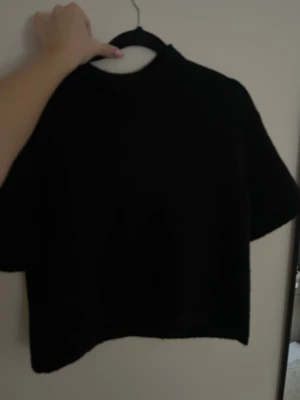 Svart stickad topp från Gina Tricot - En svart stickad topp från Gina Tricot med korta ärmar och rund hals. Enkel och stilren design som passar perfekt till både jeans och kjol. Tillverkad i mjukt material för en bekväm känsla.