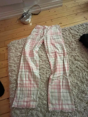 Rosa rutiga pyjamasbyxor Lindex - Mysiga pyjamasbyxor från Lindex i mjuk bomull. Byxorna har ett klassiskt rutigt mönster i rosa, vitt och grått samt resår i midjan för extra komfort. Perfekta för chillkvällar hemma eller när du vill ha det extra bekvämt.