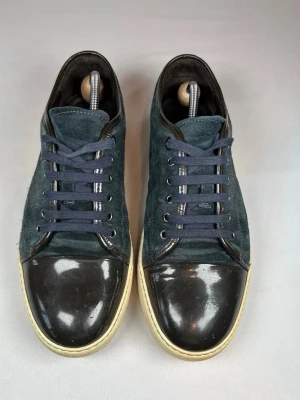 Mörkblå Lanvins med lackad tå - Snygga mörkblå sneakers med ovandel i mocka och cool lackad svart tå. Skorna har vita sulor och mörkblå snörning. Perfekta för dig som gillar en stilren men ändå unik look.