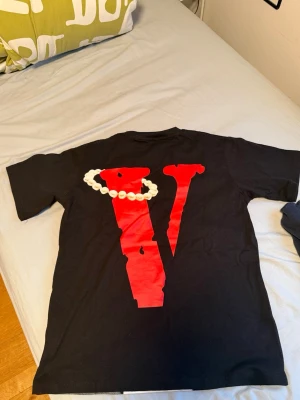 Vlone pearl tshirt - Svart t-shirt från Vlone med stort rött V och pärlgrafik på ryggen samt ett konstnärligt ansiktstryck i vitt och rött framtill. Klassisk passform och rund hals. Perfekt för dig som gillar streetwear och vill sticka ut. Helt ny aldrig använd, storlek S men oversized så skulle mer rekommendera M. Finns även vlone plastpåse och etiketten.
