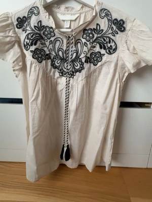 Vit blus med svart broderi och knytband - Supersöt vit blus från H&M med svart broderat blommönster. Aldrig använt 