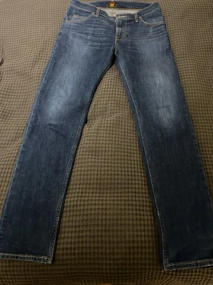 Blå raka jeans från Lee - Klassiska blå jeans från Lee med raka ben och femficksmodell. Gylf med dragkedja och Lee-lapp bak i midjan. Modell: Rider. Storlek: W30 L33. Jeansen är helt nya, inga tecken på användning.