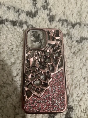 Glittrigt rosa skal till iPhone - Snyggt mobilskal med glittrig rosa nederdel och 3D-mönstrad ovandel i metallic. Skalets design har en cool kristall-liknande struktur och passar perfekt för dig som vill sticka ut. Tillverkat i plast och silikon, med öppning för kamera.