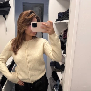 Krämvit kofta med rund hals - Mysig krämvit kofta med rund halsringning och knäppning framtill. Långärmad och i mjukt material, perfekt för lager-på-lager. Enkel och stilren design som passar till det mesta.