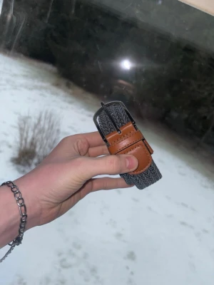 Grått flätat bälte  - Snyggt grått flätat bälte med bruna läderdetaljer vid spännet. Har bara använt bältet 2 gånger sen jag köpte. Passar till i stort sätt alla jeans.