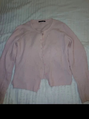 Ljusrosa kofta med knappar - Söt ljusrosa kofta med rund halsringning och knäppning framtill. Koftan har långa ärmar och en klassisk, rak passform. Perfekt att slänga över en topp för en chill look.