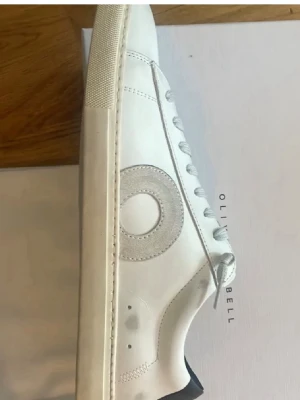 Vita sneakers från Oliver Cabell - Stilrena vita sneakers från Oliver Cabell med rund tå och platt sula. Skorna har en grå cirkeldetalj på sidan, vita snören och detaljer i skinn. Perfekta för dig som gillar minimalistisk och modern design. Skorna är i storlek 41 men är stora i storleken, passar mig som har 42,5