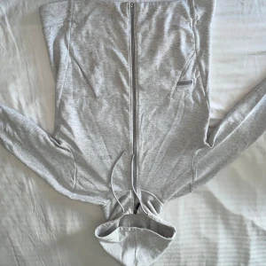 Ljusgrå hoodie från Hugo Boss - Säljer en stilren ljusgrå hoodie från Hugo Boss med dragkedja framtill, huva med snörning och diskret logga på bröstet. Tröjan har långa ärmar och praktiska fickor med dragkedja. Perfekt för en chill och clean look. Passarform är small 