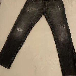Svarta jeans från Jack & Jones - Säljer ett par svarta jeans från Jack & Jones med slitna detaljer på benen.( 32-34) skulle rekomdera stort för de låga priset