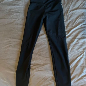 Svarta ribbade leggings från Röhnisch - Svarta leggings från Röhnisch med ribbad struktur och hög midja. Snygg och enkel design med diskret logga bak på linningen. Perfekta för träning eller chill, tillverkade i stretchigt syntetmaterial som sitter skönt hela dagen.